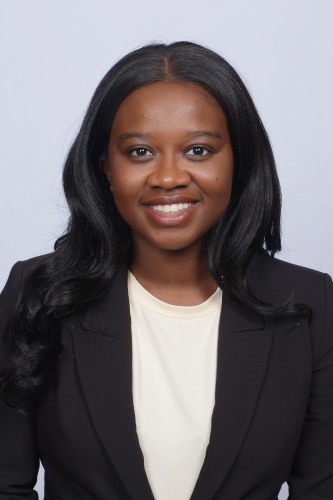 Portrait of Korede Yoloye wearing a white blouse with a black blazer against a gray background