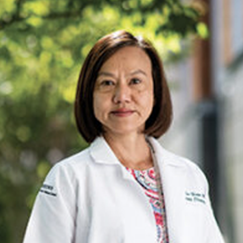 Susan Cu-Uvin's Headshot. She wears a lab coat and stands in a blurred, outdoor setting.