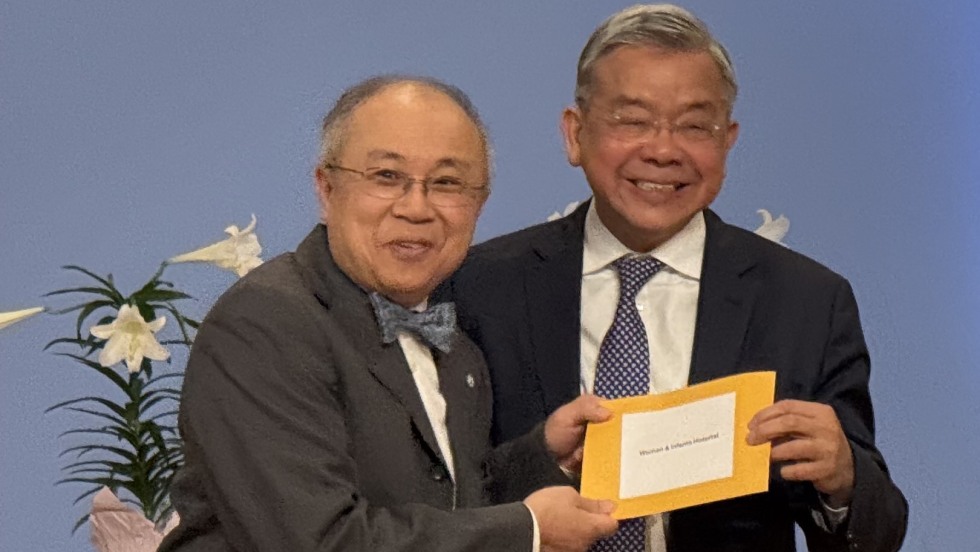 Dr. James Sung with Luke Foundation leader both standing together and smiling, holding a yellow envelope. 