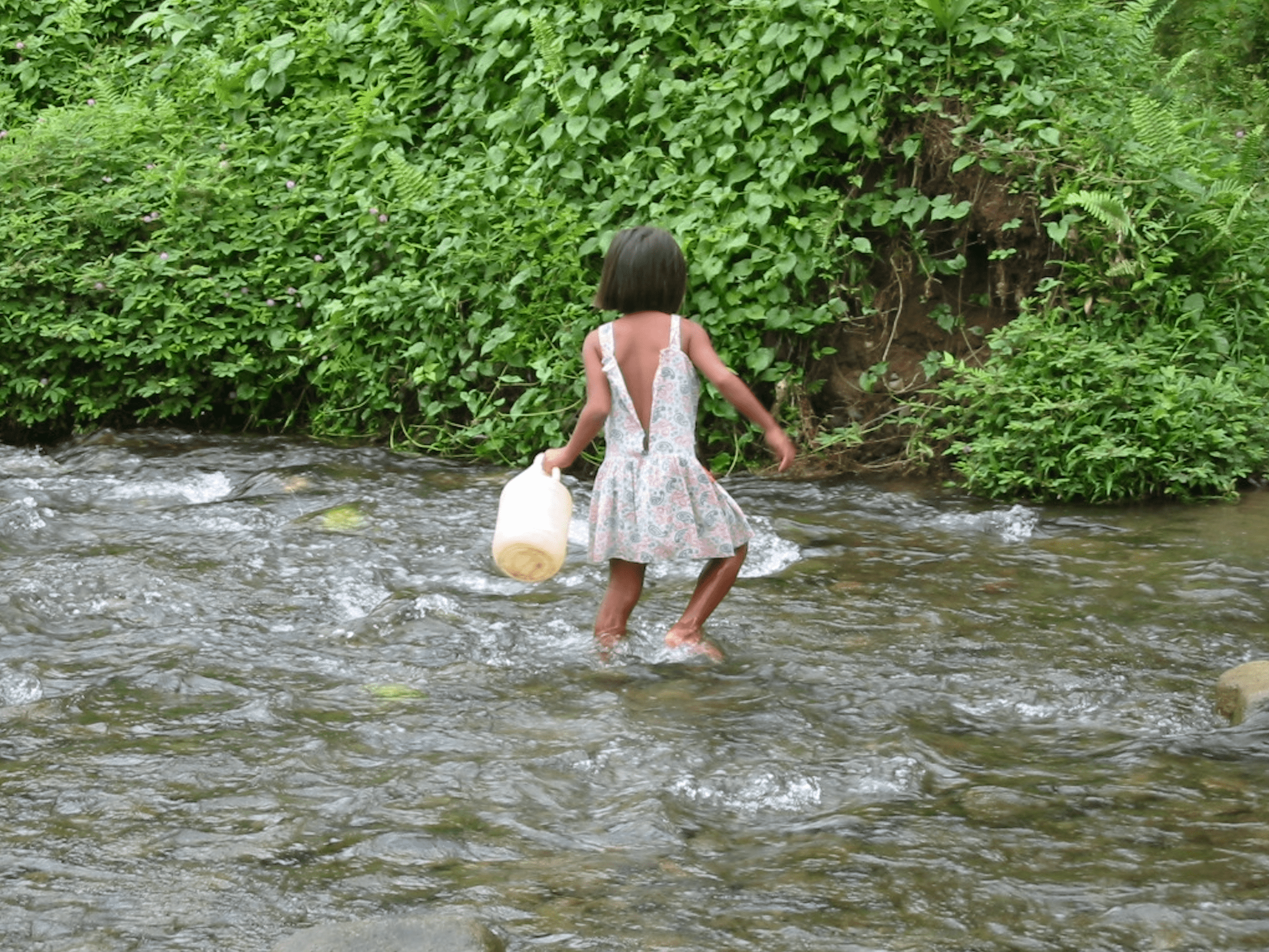 Young girl filling up a jug of water in a river.